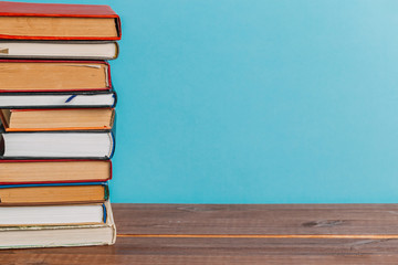A simple composition of many hardback books, raw books on a wooden table and a bright blue background. Going back to school. Copy space. Education.