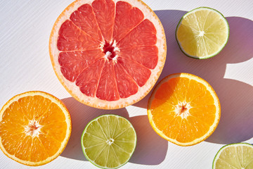 Packed ripe orange, grapefruit and lime halves packed on white wooden background, close-up shot from above in harsh sunlight with long colored shadows.