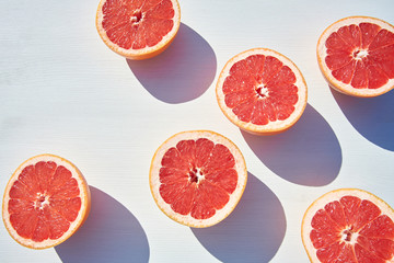 Ripe grapefruit halves loosely laid on white wooden background, shot from above in harsh sunlight with long colored shadows.