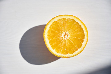 Half of ripe orange on white wooden background, close-up shot from above in harsh sunlight.