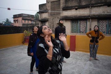 A cheerful Indian Bengali woman in winter garments enjoying by trying to catch a ball in a sunny winter afternoon on a rooftop. Indian lifestyle.