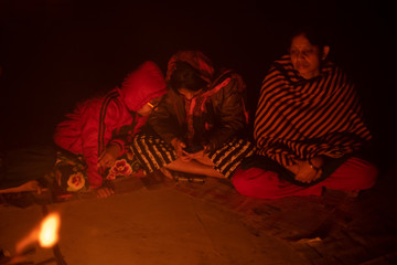 Obraz premium A cheerful Indian Bengali brunette family in winter wear enjoying bonfire on rooftop in the evening. Indian lifestyle and winter.