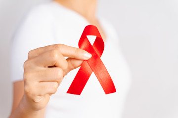 Closeup woman hand holding red ribbon HIV, world AIDS day awareness ribbon. Healthcare and medicine concept.