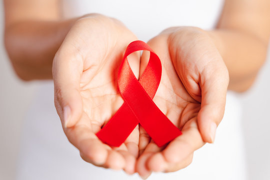 Closeup woman hand holding red ribbon HIV, world AIDS day awareness ribbon. Healthcare and medicine concept.