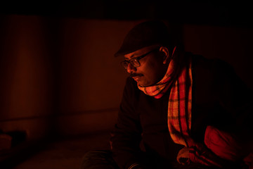 Portrait of a Indian Bengali brunette middle aged man in winter garments in a winter evening on the rooftop in front of a bonfire. Indian lifestyle.