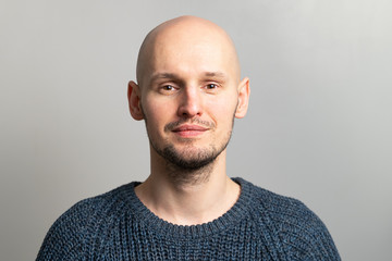 portrait of a young bald man in a knitted sweater on a gray background - obrazy, fototapety, plakaty