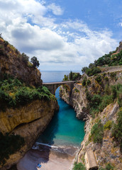 Vertical photo. Bay of Fiordo di furore beach. Incredible beauty panorama of a mountains paradise. The rocky seashore of southern Italy. Sunny day. Stone bridge and clear water. Amalfi coast. - obrazy, fototapety, plakaty