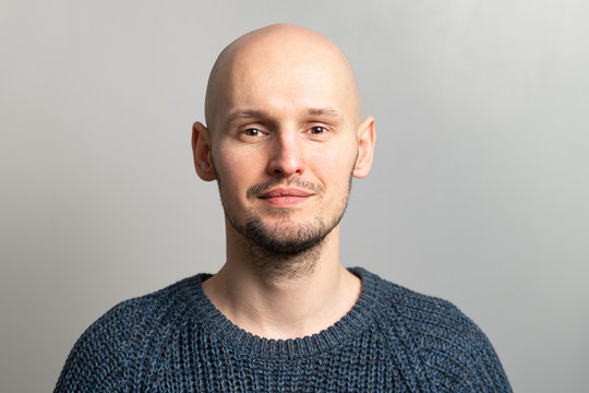 portrait of a young bald man in a knitted sweater on a gray background