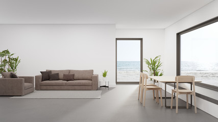 Table on concrete floor of large dining room near living area and sofa in modern beach house or luxury hotel. Minimal home interior 3d rendering with sea view.