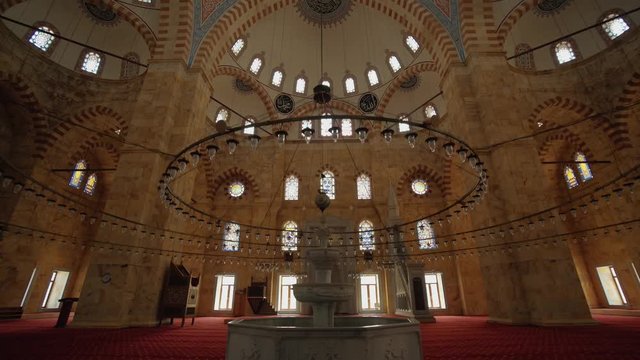 Interior view of the domed mosque with lots of windows. large chandelier and fountain inside. with red carpet.