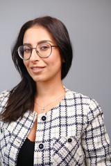 Portrait of a smiling mid-aged business woman with dark hair and brown eyes in glasses and a jacket against a light wall