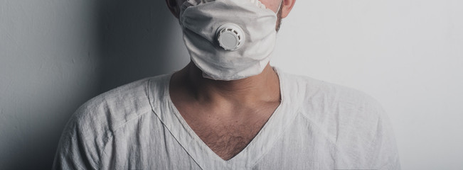 A young man in a quarantined hospital wearing a respiratory mask and hospital clothing,