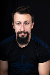 Obraz premium a close up portrait of a young man with beard in dark clothes on a dark background