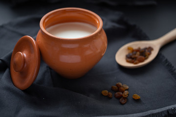 Brown pot with sour cream and a wooden spoon with raisins on a dark background.