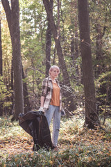 A young girl - an eco activist collects trash and plastic in a park and forest stacks up in a black big bag. Clean eco system concept