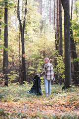 Fototapeta premium A young girl - an eco activist collects trash and plastic in a park and forest stacks up in a black big bag. Clean eco system concept
