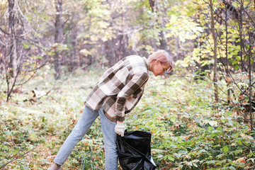 A young woman - an eco activist collects trash and plastic in a park and forest stacks up in a black big bag. Clean eco system concept