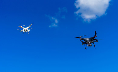 Modern drons flying above city. White and dark quadrocopters in sky.