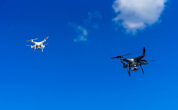 Modern drons flying above city. White and dark quadrocopters in sky.