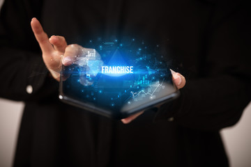 Businessman holding a foldable smartphone with FRANCHISE inscription, business concept