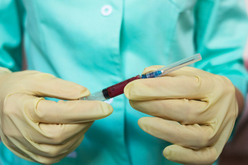 Hand of a female doctor in a green coat and medical glove holding a syringe with blood for testing in a hematology laboratory in a hospital, closeup. The concept of medicine