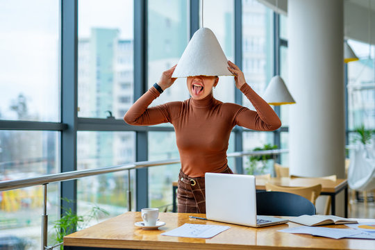 Woman With A Lampshade On Head Standing In Business Office. Brainstorming Concept.