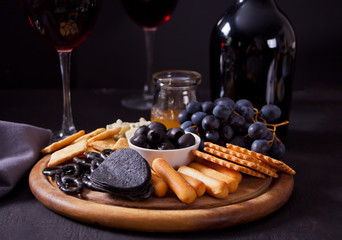 Glasses of red wine, bottle and plate with assorted cheese, fruit and other snacks for party