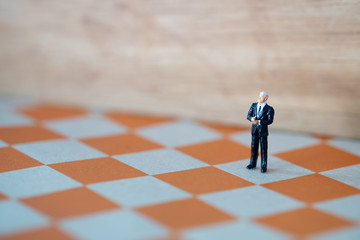 Miniature people: Businessman standing on the chess game