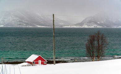Hvaloya, Tromsø / Norway - March 6th, 2020: A wooden house on the banks of the Arctic Ocean in a snowy scenery in Hvaloya Island near Tromsø