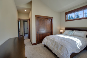 Bright new natural tones bedroom with queen size bed with grey carpet and three windows,