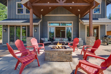 Back yard with fire pit and red chairs near newly bild luxury real estate home with forest biew and green grass.