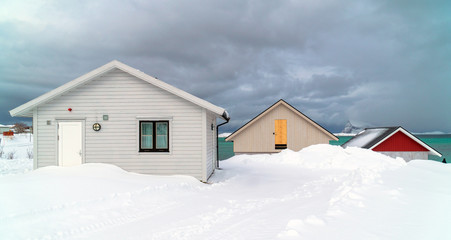Sommarøy, Tromsø / Norway - March 6th, 2020: Three traditional wooden houses under the snow and a cloudy sky at Sommarøya Island in winter
