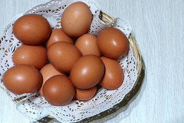 brown eggs lie on a lacy, white napkin, in a basket, on a background of light wood. Easter light cooking