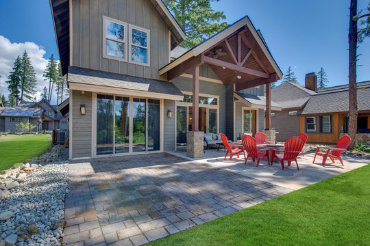 Back yard with fire pit and red chairs near newly bild luxury real estate home with forest biew and green grass.
