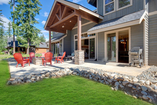 Back yard with fire pit and red chairs near newly bild luxury real estate home with forest biew and green grass.