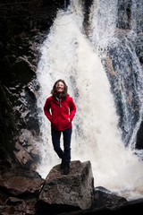junge Frau steht mit roter Regenjacke vor einem Wasserfall im Schwarzwald