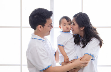 Fototapeta premium Asian young family together feeding adorable cute girl at home, father making small business marketing online logistic home office, mother playing with the child, parenthood duty multi task concept