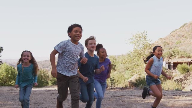Camera tracks group of multi-cultural children with friends runnIng towards camera in countryside together - shot in slow motion