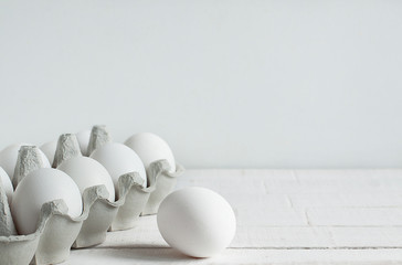 White raw chicken eggs in a cardboard box on a white background. Separately, one egg in front of the box. Organic food for good health, high protein levels