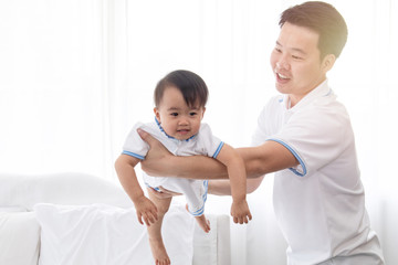 Asian young family help together feeding adorable cute girl at home, father playing with daughter hold her to fly on bed, mother pregnancy looking beloved husband and daughter multi task concept