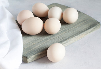 Close- up view of fresh raw chicken eggs on a wooden Board with a textile napkin. One egg in front of the Board . Natural healthy food. High protein content