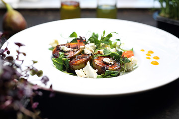 Caramelized figs on lettuce with goat cheese. A plate with an appetizing dish. Application suggestion. Culinary photography, food stylization.