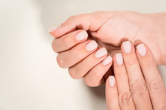 Closeup top view of two beautiful hands of woman with professional manicure, nails painted with light pink color and covered with matte top without glossy shine. Nude style design of fingernails.