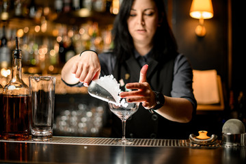 Bartender pouring ice cubes into glass on bar counter.