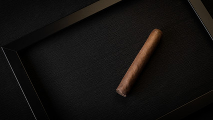 One cigar in a black frame on a black background. Abstraction and minimalism.