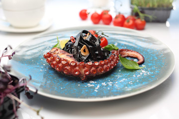 Pasta with octopus. Black spaghetti with squid ink. A plate with an appetizing dish. Application suggestion. Culinary photography, food stylization.