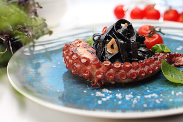 Black pasta with octopus. A plate with an appetizing dish. Application suggestion. Culinary photography, food stylization.