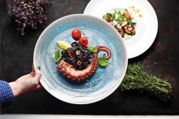 Pasta with octopus. Tagliatelle black colored with squid ink.A plate with an appetizing dish. Application suggestion. Culinary photography, food stylization.
