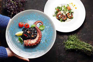 Pasta with octopus. Black spaghetti with squid ink. A plate with an appetizing dish. Application suggestion. Culinary photography, food stylization.