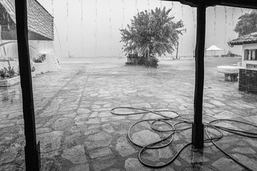 Black and white photography of heavy rainstorm pouring outdoors at empty  beach of hotel resort in Greece.